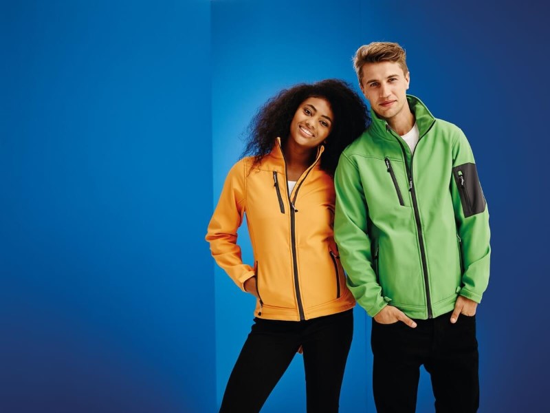 Modelos con chaquetas Soft Shell promocionales en colores verde y naranja, mostrando su estilo moderno y versatilidad