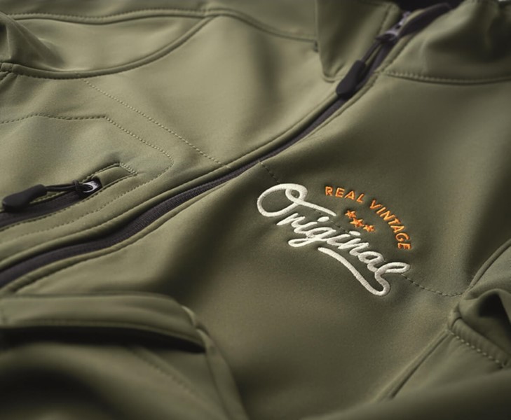 Detalle de bordado en una chaqueta Soft Shell promocional verde con logotipo personalizado, mostrando la calidad del tejido y los acabados