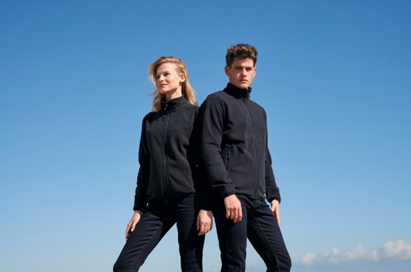Pareja de modelos con chaquetas Soft Shell promocionales negras, representando comodidad y resistencia para actividades al aire libre y profesionales